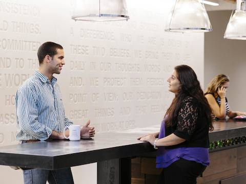 Two people converse at a high-top table while another talks on a phone.