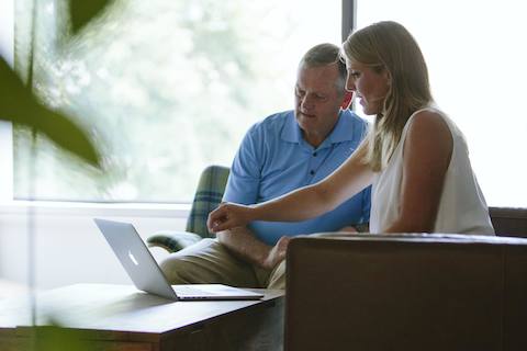 Two people look at a computer screen while sitting in lounge area with natural light.