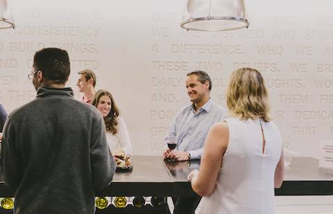 People stand and drink wine at a high-top table. 