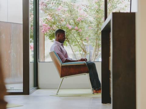 A man sits in a Swoop lounge chair while looking at his laptop.