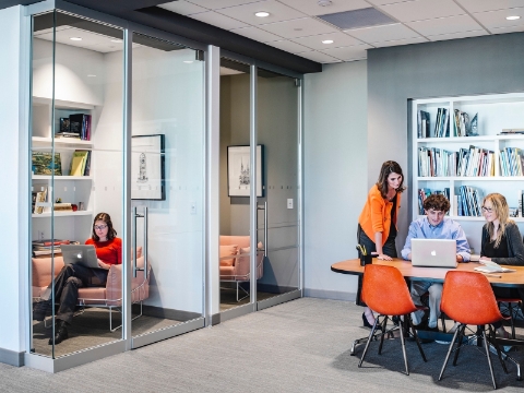 People work and discuss amidst open office areas and closed off rooms with glass walls. 