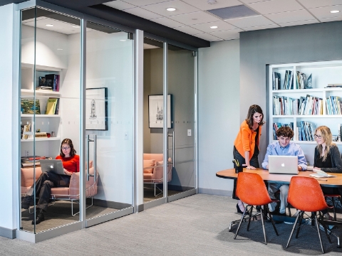 People work and discuss amidst open office areas and closed off rooms with glass walls. People work and discuss amidst open office areas and closed off rooms with glass walls.