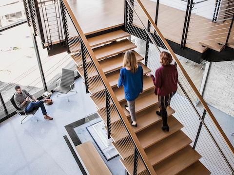 Two women make their way up a staircase as a man sits down below. 