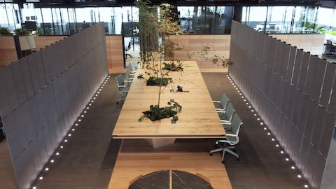 Six sièges Setu garnis de tissu, disposés autour d’une table en bois personnalisée, avec de vrais arbres à l'intérieur pour intégrer la nature à l’environnement de travail. Des panneaux mobiles garnis de tissu de Brinco font office de parois latérales et contribuent ainsi à ajuster la lumière naturelle.