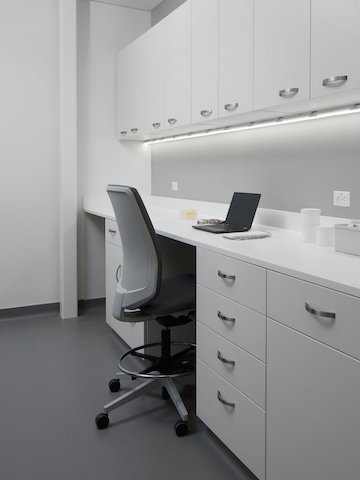 Laboratory workspace with white Mora casework for upper and lower cabinets and a Verus stool in a gray upholstery.