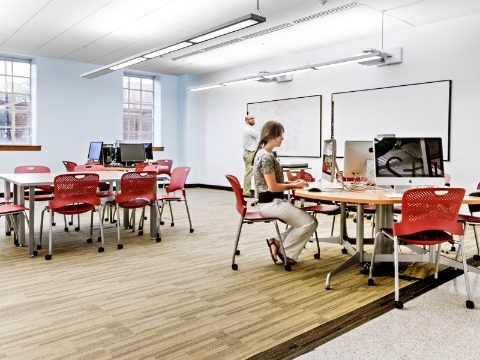 A student sits typing on a computer while an instructor writes on a white board. 