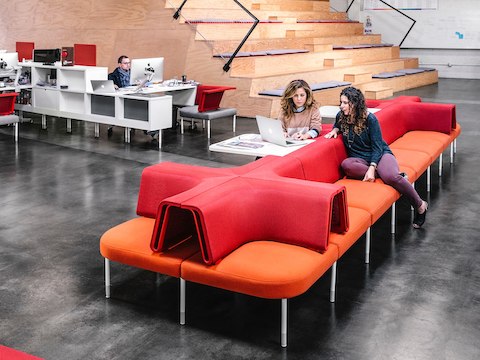 People work and discuss projects while seated at a desk and lounge sofas. 