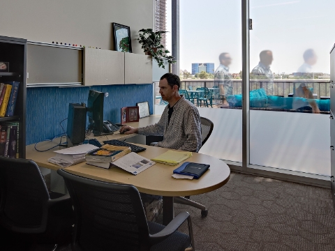 A faculty member works at his computer inside of his office area. 