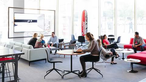 People working and meeting in a lobby space next to windows.