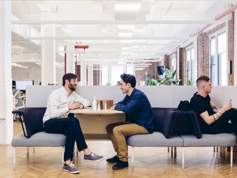 Two men in lounge seating converse while another sits nearby. 