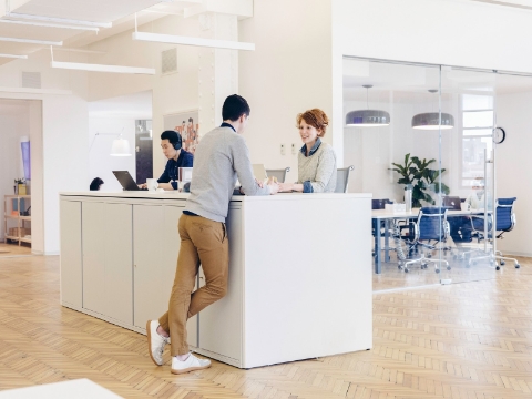 Office employees work and talk at an extended desk setup. 