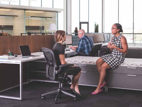 Employees work and converse while seated in an open office environment. Employees work and converse while seated in an open office environment.