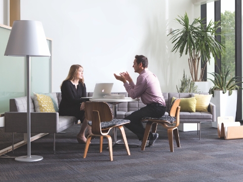 Two people sit and talk in an office lounge area.