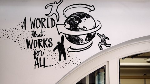 An illustration along a wall of three people and the world. An illustration along a wall of three people and the world.
