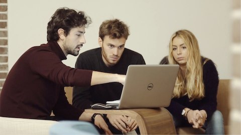 Zwei Männer und eine Frau, die Arbeit an einem Beistelltisch begutachten.