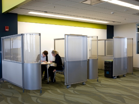 Two women seated in Caper chairs work inside a semi-private meeting space.