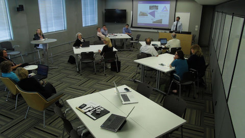 Students have a discussion with an instructor amongst Everywhere tables and Caper chairs.