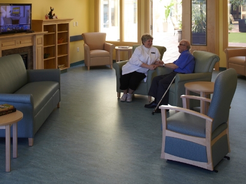 A staff member visits with a resident of an assisted living center inside a T.V. room. 