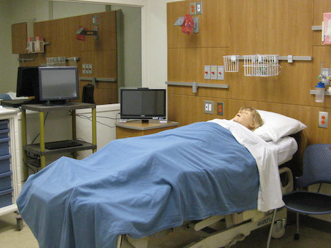 A manikin lies inside of a simulated patient room for healthcare students. 