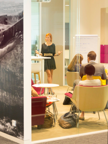 Standing and seated co-workers interact in a casual meeting space.