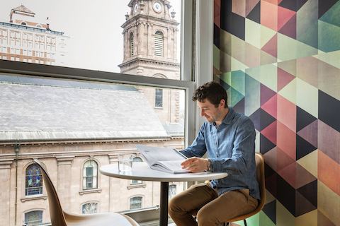 A man sits near a large window while reading a book. 