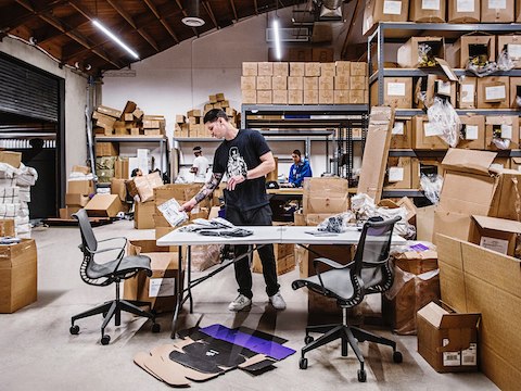 A man sorts through products at a desk inside of a warehouse area. 