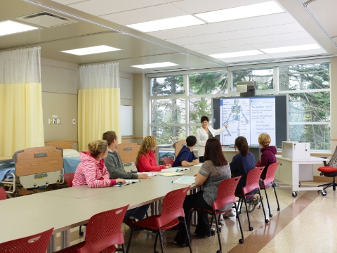 Nursing students seated in Caper chairs watch as a teacher explains a diagram.