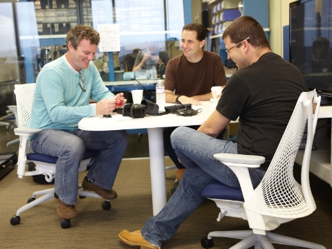 Three men sit in Sayl chairs while conversing at a table. 