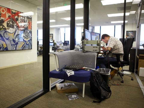 A man focuses on his work while inside of a glass-walled office space. 