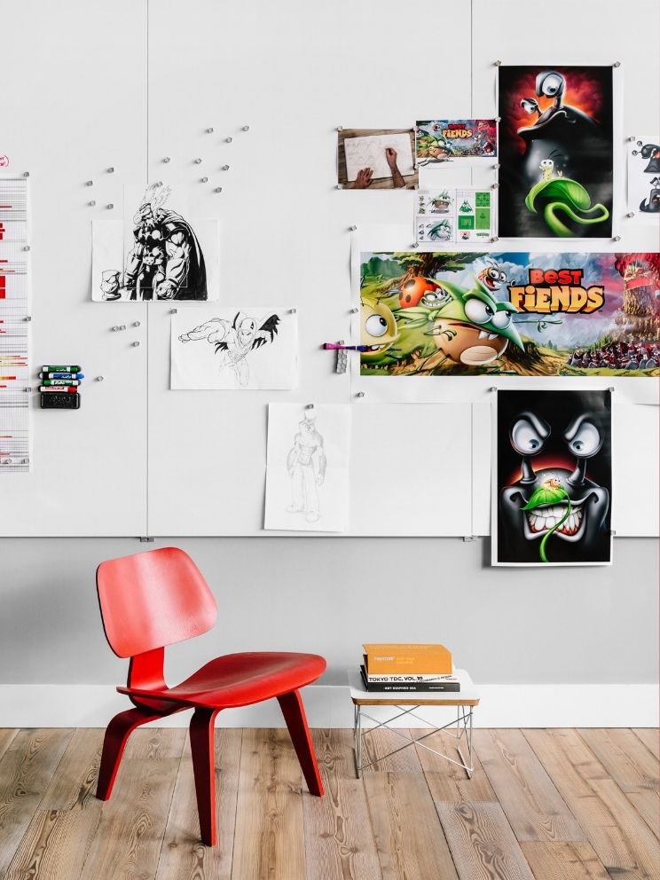 An office wall full of sketches and various illustrations behind a wood chair. 