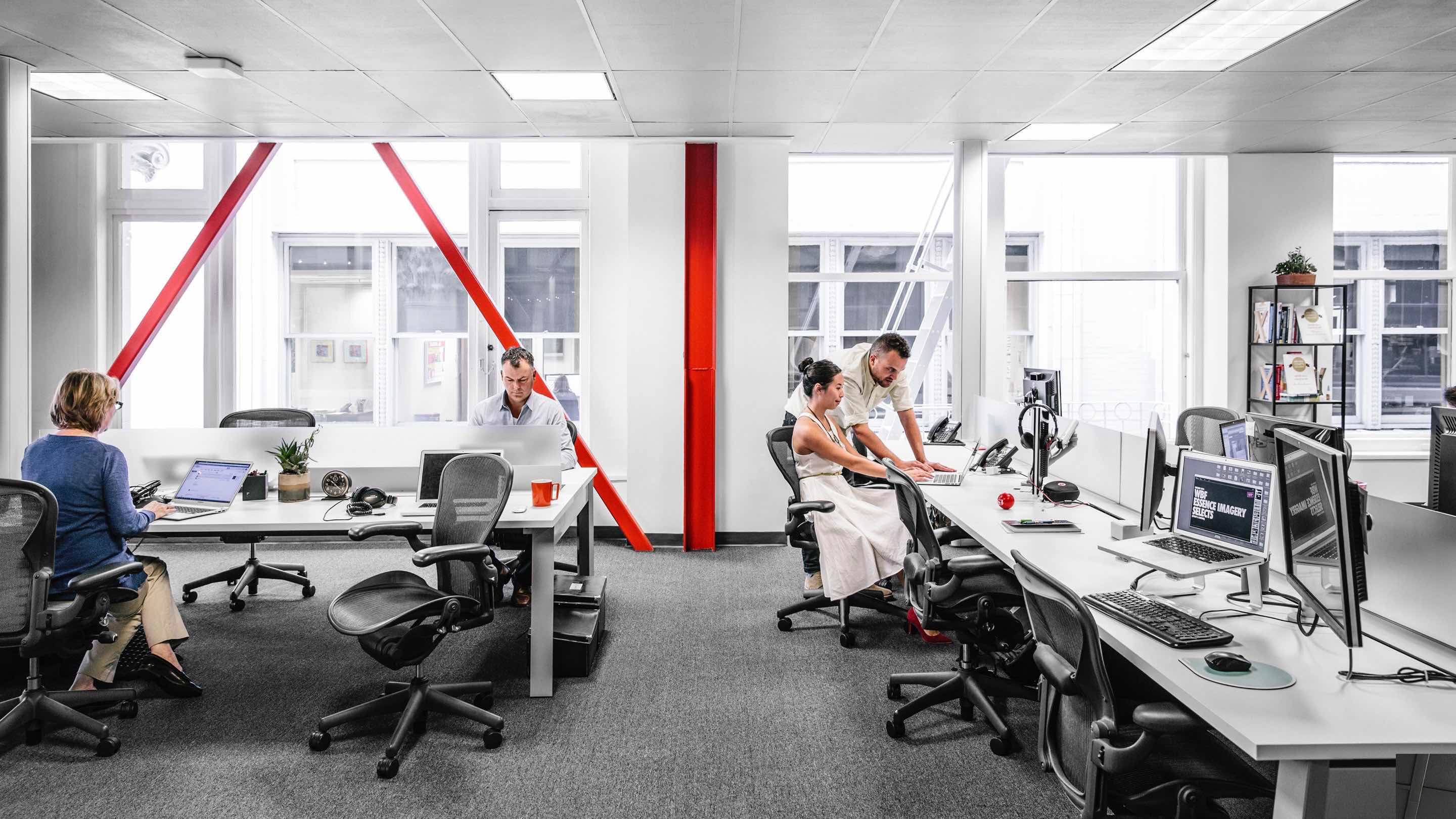 Employees work inside an open office environment with bold red highlights. 