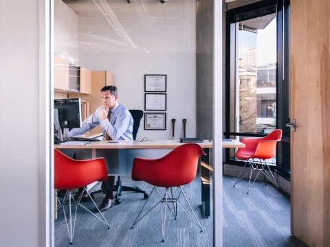 A man works at his office computer with three Eames molded chairs nearby. 