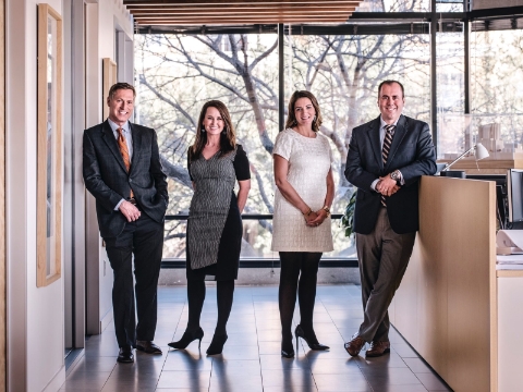 Four people pose in front of a window inside their office space. 