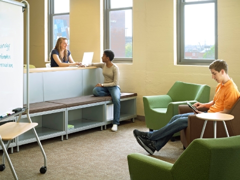 Students study and converse while seated in different furnishings throughout a classroom area. 