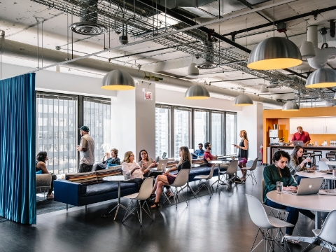 Employees talk and work while spread throughout a communal office setting. Employees talk and work while spread throughout a communal office setting.
