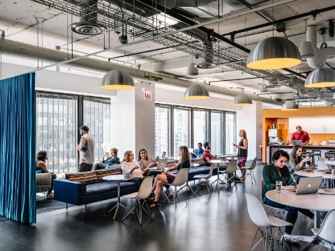 Employees talk and work while spread throughout a communal office setting. 