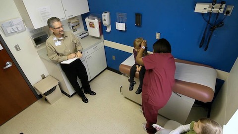 A health professional examines the ear of a young girl while others look on. 