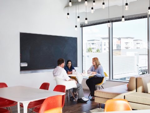 Office employees sit in Eames chairs and converse at a table. 