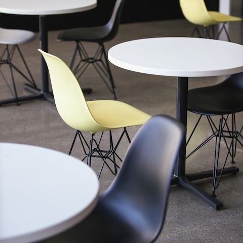 A close crop of three circular white-topped Everywhere Tables surrounded by yellow and black Eames Molded Plastic Shell Chairs.