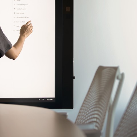 A view of a person's arm as they interact with the large touchscreen in a conference room with white Sayl Stools.