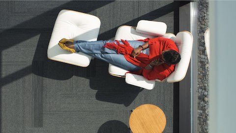 Woman sitting in a window in a White Leather Eames Chair with matching ottoman.