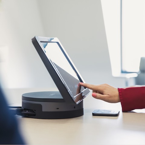 A close up of a hand tapping a touchscreen to set up the room for a video conference.