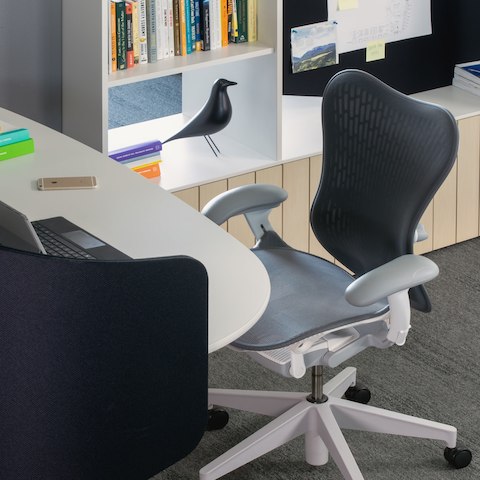 A workstation with a white Locale desk and a gray and white Mirra 2 Chair and Locale bookshelf with decor in the background.
