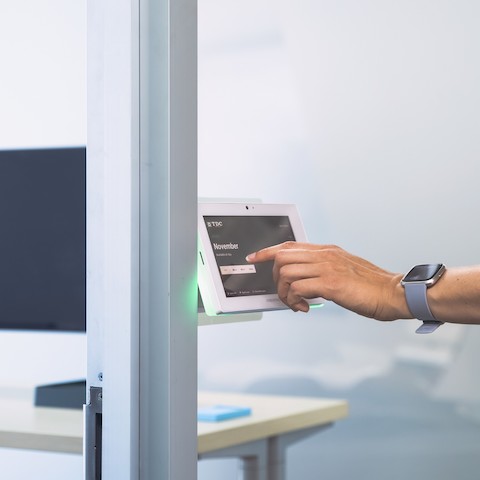 A close up of a person's hand tapping the screen of a Robin room scheduling device mounted to the outside of the private office. 