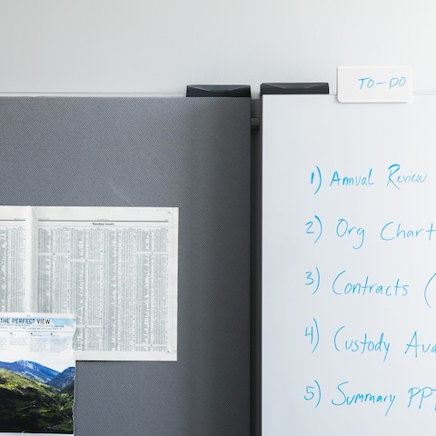 An Exclave whiteboard with writing in blue and a gray tackboard with papers and pictures pinned to it.