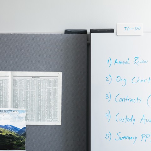 An Exclave whiteboard with writing in blue and a gray tackboard with papers and pictures pinned to it. An Exclave whiteboard with writing in blue and a gray tackboard with papers and pictures pinned to it.