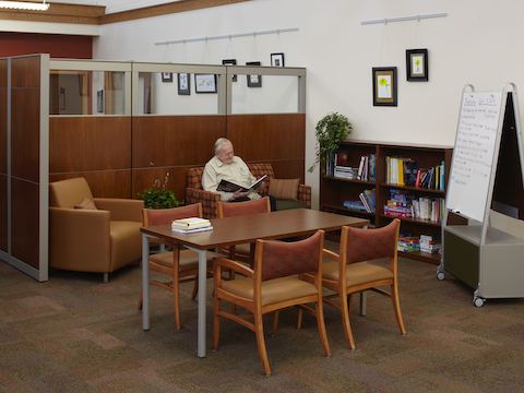 A man reads a book while seated inside of a small library area. A man reads a book while seated inside of a small library area.