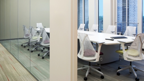 A glass-walled meeting room with Sayl chairs and a large conference table. 