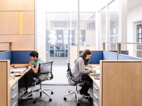 Two students study while seated at desks that offer privacy. Two students study while seated at desks that offer privacy.