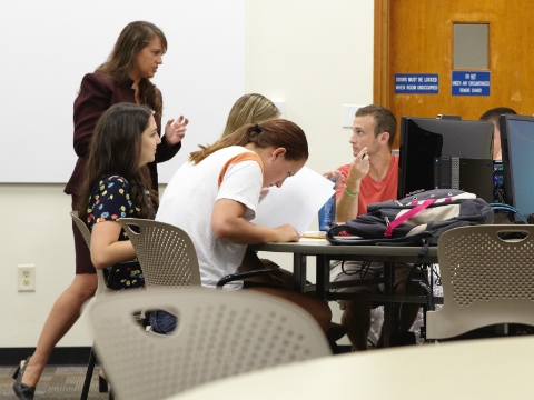 An instructor talks to a small group of seated students during a class. An instructor talks to a small group of seated students during a class.